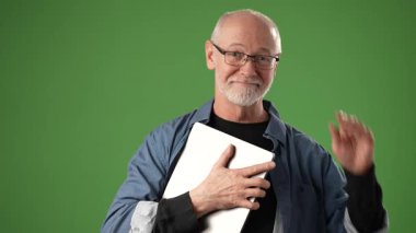 Olgun bir adam dizüstü bilgisayarla poz verir, canlı yeşil bir arkaplan karşısında durarak güvenle gülümser. İfadesi iyimserliği ve anonslara hazır olmayı gösteriyor..