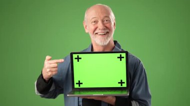 Olgun bir adam stüdyoda duruyor, yeşil ekranlı bir dizüstü bilgisayarı işaret ederken gülümsüyor. Profesyonel bir ortamda girişimciliğin ruhunu somutlaştırıyor..
