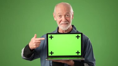 Olgun girişimci elinde parlak yeşil ekranlı, izleme noktaları olan bir dizüstü bilgisayar tutuyor, gülümsüyor ve iyi aydınlatılmış bir stüdyoda olumlu bir çalışma alanı atmosferi sergiliyor..