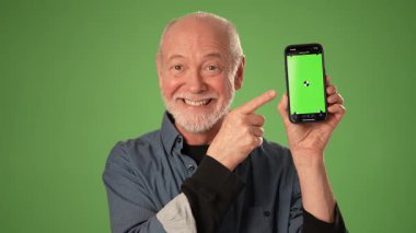 Gülümseyen olgun bir adam yeşil ekran arkaplanı olan akıllı bir telefonu işaret ediyor. Reklamcılık ya da tanıtım duyuruları için ideal..