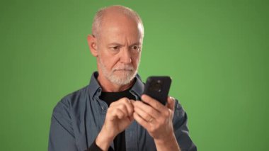 Olgun bir adam, akıllı telefonuna bakarken gülümser ve onaylar. Sağlam yeşil bir arkaplanı vardır. Anonslar ve promosyonlar için mükemmeldir..