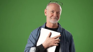 Üst düzey bir adam dizüstü bilgisayarı yakın tutarken sıcak bir şekilde gülümser. Yeşil ekran çeşitli duyurular veya ürün promosyonları için sağlam bir arkaplan sağlar.