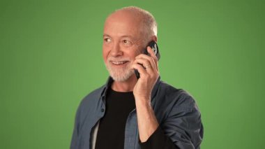 Sakallı olgun bir adam, yeşil arka planda telefonla konuşurken gülümsüyor. Duygularını dile getiriyor ve önemli bir duyuru yapıyor..