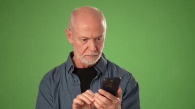 Olgun bir adam, elinde akıllı bir telefonla sevinçle tepki verirken heyecan gösterir. Katı yeşil arka plan onun anlamlı portresine odaklanıyor..