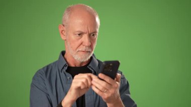 Olgun bir adam, duyurular ya da terfiler için katı yeşil bir ekranda izole edilmiş akıllı telefonunu kullanırken öfke ve hayal kırıklığını ifade eder..