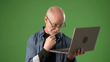 Gözlüklü son sınıf öğrencisi, bir dizüstü bilgisayar kullanmaya odaklanıyor. Duygu ve bağlılık duygusunu açık yeşil ekran bir arka plana yansıtıyor. Duyurular için ideal..