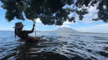 Mutlu bir gezgin, Ometepe Adası 'nın arka planında Concepcion volkanı görkemli bir şekilde yükselirken, bir gölün sakin sularında sallanmaktan zevk alır..