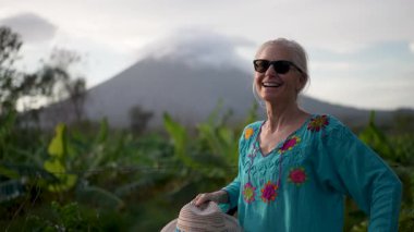 Olgun kadın portresi Nikaragua 'daki Ometepe Adası' nda bisiklet sürmekten hoşlanıyor. Arkaplanda Concepcion volkanı belirir ve bölgenin doğal güzelliğini vurgular. Gülümserken başparmağını kaldırır.,
