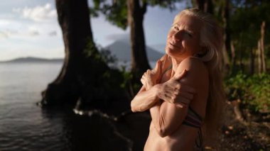 Güzel, olgun bir kadının portresi sakin gölün yanında duruyor, kollarına sarılmış, sıcak bir şekilde gülümsüyor, güneş bir volkanın arkasında batarken, Orta Amerika 'da huzurlu bir atmosfer yaratıyor..