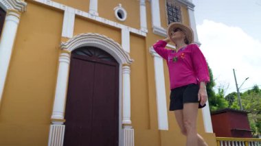 Rengarenk yürüyüşler yapan mutlu bir kadın Moyogalpa, Ometepe Adası 'ndaki canlı bir kilisenin yanından geçerken Orta Amerika' nın neşeli atmosferini yakalıyor..