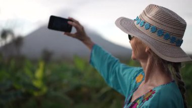 - Yakın çekim. Renkli kıyafetli, gülümseyen olgun bir kadın, Nikaragua 'daki Ometepe Adası' nda Concepcion Volkanı 'nda bisiklet sürerken telefonuyla fotoğraf çekiyor. Neşeli macerasının tadını çıkarıyor..