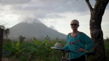 Olgun bir kadının portresi, Nikaragua 'daki Ometepe Adası' nda bisiklet sürerken, güzel bir günde arka planda muhteşem bir Concepcion volkanı ile başparmağıyla gülümsüyor..