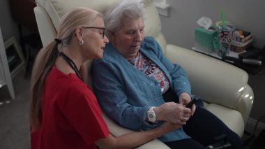 Bir bakıcı, aydınlık ve rahat bir oturma odasında, aydınlık ve rahat bir oturma odasında, yaşlı bir kadına yardım eder..