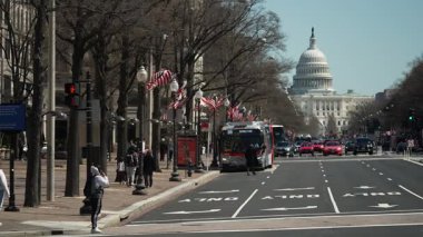 Washington, D.C. 'deki ABD Kongre Binası yakınlarında yürüyen bir belediye otobüsü ve yayaların yer aldığı işlek sokak manzaraları bulvarda sıra sıra dizilen ağaçlarda sergileniyor..