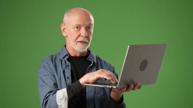 Stüdyoda dizüstü bilgisayar tutarken mutsuz bir şekilde el kol hareketi yapan sinirli olgun bir adamın portresi. Yeşil ekranda izole edilmiş bir adam çok yönlü içerik oluşturma ve düzenlemeye izin verir.