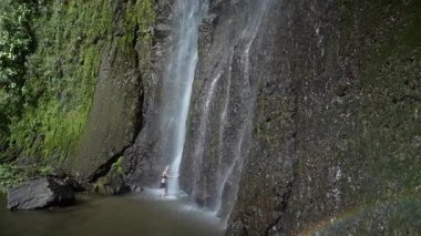 Olgun bir kadın, Nikaragua, Ometepe Adası 'ndaki San Ramon şelalesinin ferahlatıcı sularında yürüyor. Etrafı yemyeşil ormanlarla çevrili ve Orta Amerika' da canlı bir gökkuşağı var..