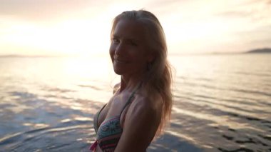 Gülümseyen orta yaşlı kadının yakın plan portresi gün batımında Orta Amerika gölünün sakin sularında duruyor. Tatilinin güzelliğini kucaklayarak neşe saçıyor..