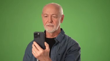 Kıdemli girişimci, arkadaşları ve iş arkadaşlarıyla birlikte canlı yeşil ekran arka planına sahip bir stüdyoda canlı bir atmosfer yaratarak akıllı telefonunda neşeli bir şekilde görüntülü sohbet ediyor..