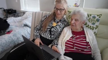 Bir kız, yaşlı annesiyle rahat bir oturma odasında görüntülü konuşma yaparken gülümsüyor. Sıcak atmosfer, yakın bağlarını ve bağlantılarını yansıtıyor..