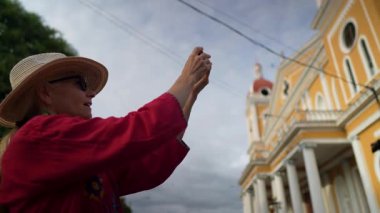Hasır şapkalı olgun bir kadın, güneşli bir günde şehrin renkli mimarisinin fotoğraflarını çekerek Granada, Nikaragua 'da eğleniyor..