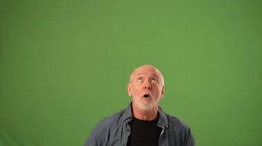 Olgun bir adam, güçlü duygular ve enerji iletirken, iki eli havada, yeşil bir zemine doğru bakarken neşeli bir şekilde el kol hareketi yapar..