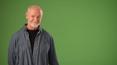 Yaşlı adam yeşil bir zeminin önünde dururken nazikçe gülümsüyor, çeşitli ürün duyuruları için uygun davetkar bir ortam yaratıyor..