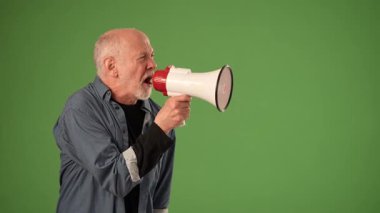 Olgun bir adam, bir duyuru yapmak için megafon kullanarak kendinden emin bir şekilde ayakta duruyor. İfadesi güçlü duygular gösteriyor, mesajın önemini vurguluyor..