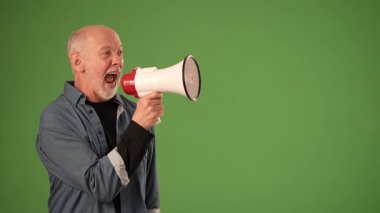 Olgun bir adam yeşil ekranın önünde duruyor, megafon kullanırken heyecanını ifade ediyor, çeşitli duyurular ve promosyonlar için uygun..