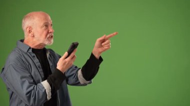 Olgun bir adam akıllı telefonunu kullanırken duygusal bir tepki gösterir. Katı yeşil arka plan çeşitli duyurular veya ürünler için çok yönlülük sunar.