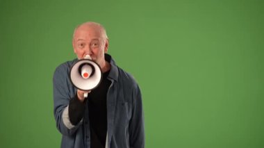 Olgun bir adam elinde bir megafon tutarken heyecanını ifade eder. Promosyon içeriği için mükemmel bir yeşil arkaplan karşısında duyuru yapmaya hazırdır..