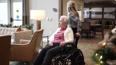 Columbia, MD, ABD - 12252024: Tekerlekli sandalyedeki yaşlı bir kadın, aile ziyaretleri sırasında sevgi ve bağlılık anlarını yansıtan, kızıyla bir bakımevinde vakit geçiriyor.