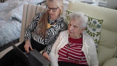 Yaşlı bir kadın ve kızı bir dizüstü bilgisayarla görüntülü sohbete bağlanırken, sıcak bir oturma odasında ailecek vakit geçirmenin keyfini çıkarıyorlar..