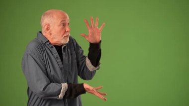 Gri saçlı ve sakallı neşeli bir son sınıf öğrencisi yeşil ekrana karşı heyecanla ellerini kaldırıyor. Neşeli ifadesi olumlu duygular ve coşku taşıyor..