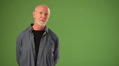 Olgun bir adam yeşil bir zemine karşı gururla durur. Sıcak bir gülümseme ve kendine güvenen bir duruş sergiler. Ürün duyurusu için mükemmel bir duruştur..