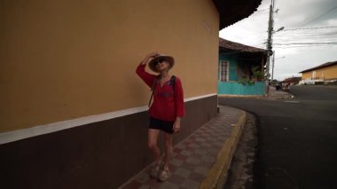 Granada, Nikaragua 'da renkli bir duvara karşı duran bir kadın şık bir şapka ve günlük kıyafetler giyerek kasabaların hareketli atmosferinin tadını çıkarıyor..