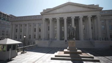 Washington, DC, ABD - 03 21 2025: Hazine Bakanlığı Washington DC 'de bahar güneşiyle aydınlanan bir binadır. Öndeki bir heykel, federallere tarihsel bağlam katıyor.