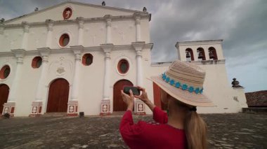 Olgun bir kadın, Granada, Nikaragua 'da dramatik bir gökyüzüyle çevrili güzel bir manastırın fotoğrafını çekiyor. Bu onun Orta Amerika 'daki seyahat deneyimini vurguluyor..