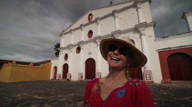 Canlı atmosferin tadını çıkaran olgun bir kadın, Granada, Nikaragua 'daki çarpıcı manastırın önünde durup Orta Amerika' nın özünü yakalıyor..