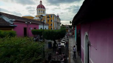 Granada, Nikaragua - 0104 2025: Ziyaretçiler bulutlu bir günde etkileyici bir katedral olarak hizmet veren Granada, Nikaragua 'daki Calzada' da Calle La Calzada boyunca yemeğin tadını çıkarıyorlar..