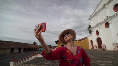 Olgun bir kadın, Nikaragua Granada 'daki güzel bir manastırın önünde neşeli bir oto portre çekiyor. Titreşimli atmosfer, tarihi ve onun neşeli ruhunu birleştiriyor..