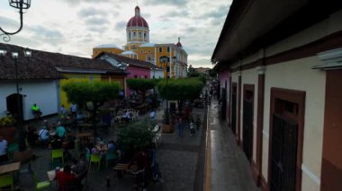 Granada, Nikaragua - 0104 2025: Ziyaretçiler Calzada yakınlarındaki hareketli restoran ve kafelerde toplanarak, arka planda katedral bulunan Granada, Nikaragua 'nın canlı atmosferini gözler önüne seriyorlar..