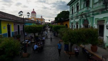 Granada, Nikaragua - 0104 2025: Ziyaretçiler Granada, Nikaragua 'da Calzada boyunca geziniyor, yerel mutfağın ve arka plandaki büyüleyici katedralin keyfini çıkarıyorlar bulutlu bir gökyüzünün altında..