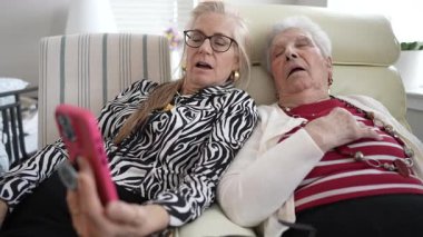 80 'li ve 90' lı yaşlarda iki yaşlı kadın görüntülü bir sohbete girişiyor. Birlikte rahat bir şekilde otururlar, akıllı telefon kullanırken gülücüklerini ve gülüşlerini paylaşırlar..