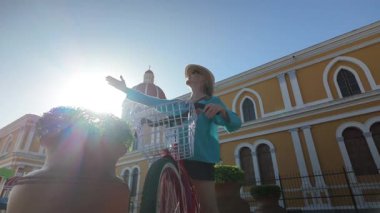 Turist bir kadın bisikletçilik deneyimini Nikaragua, Granada 'da kutluyor. Arka planda açık gökyüzünün altında güzel bir katedral var..