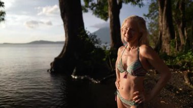 Çekici, mutlu, olgun bir kadının portresi Nikaragua 'da bir gölde bikini giyer ve Concepcion volkanı tarafından tatili boyunca sıcak gün batımını ve doğal güzelliği kucaklar..