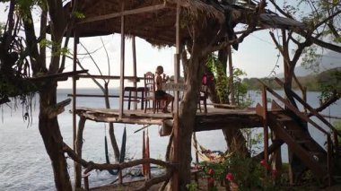 Orta yaşlı bir kadın, Ometepe Adası ve Concepcion yanardağının orman manzarasıyla çevrili, ahşaptan yapılmış bir restoranda smoothie yudumlarken gülümsüyor..