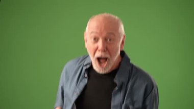 Tedirgin bir ifadeye sahip olgun bir adam, yeşil bir arka planın önünde dikilirken yüzünü elleriyle kapatır ve bir sıkıntı hissi taşır..