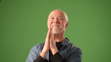 Olgun bir adam, yumuşak bir gülümseme ile kendini kucaklıyor, derin bir sıcaklık ve neşe iletiyor, katı yeşil bir arka plan üzerine kurulmuş. Kendini sev.