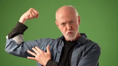 Sakallı olgun bir adam yeşil bir arka fonun önünde dikilirken kalemini düşünceli bir şekilde tutuyor. Düşünceli bir ifade sergiliyor, merak uyandırıyor..