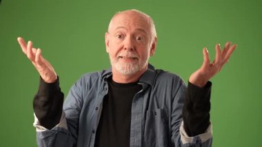 Olgun bir adam, yoğun bir duygu sergiliyor. Şaşırmış bir ifadeyle, elleri başının üstünde, katı yeşil bir ekranın önünde..